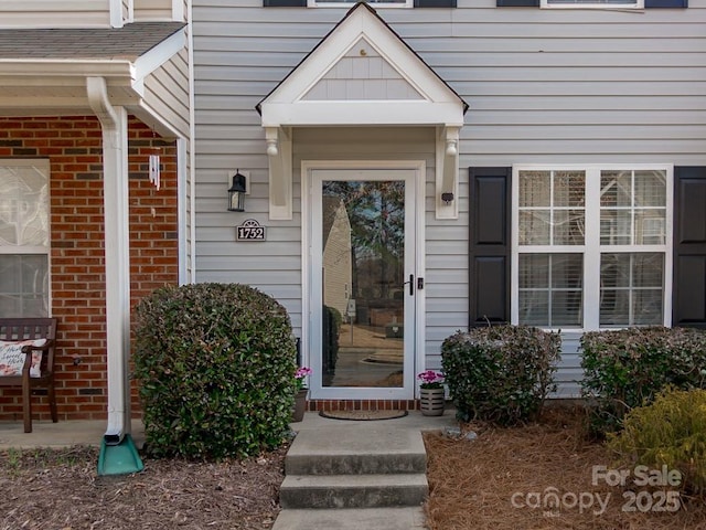 doorway to property with a shingled roof and brick siding