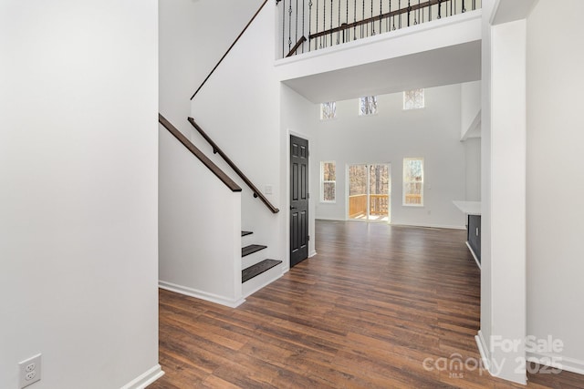 foyer entrance with a high ceiling, stairs, baseboards, and dark wood-style flooring