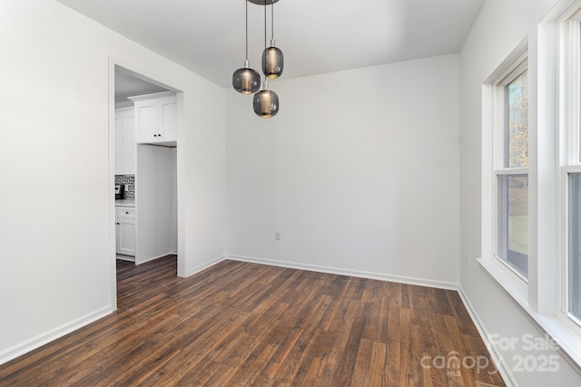 unfurnished dining area featuring dark wood-style flooring and baseboards