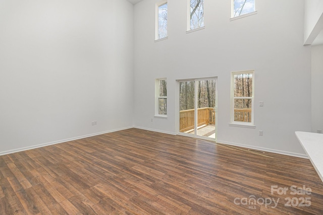 unfurnished living room featuring dark wood finished floors, a towering ceiling, and baseboards