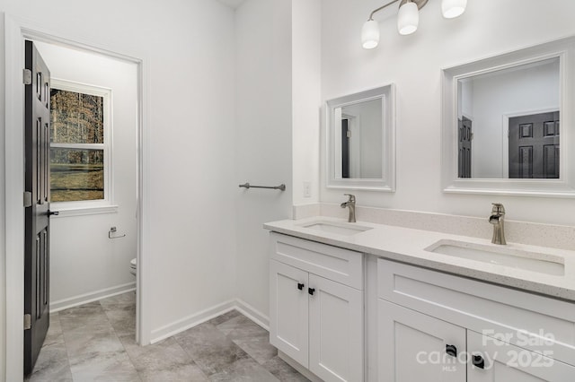 bathroom with double vanity, a sink, toilet, and baseboards