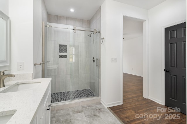 full bathroom with double vanity, a shower stall, baseboards, and a sink