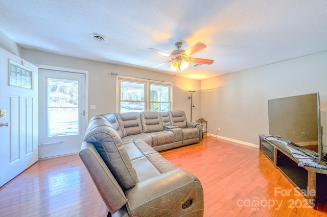 living area featuring a textured ceiling, a ceiling fan, baseboards, visible vents, and light wood-style floors