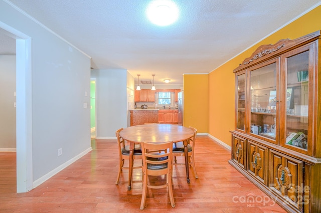 dining area with light wood-type flooring, crown molding, a textured ceiling, and baseboards