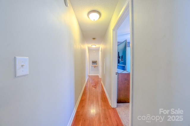 hallway featuring a textured ceiling, baseboards, and light wood-style floors