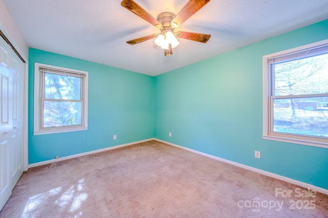 carpeted spare room with baseboards, a textured ceiling, a ceiling fan, and a healthy amount of sunlight