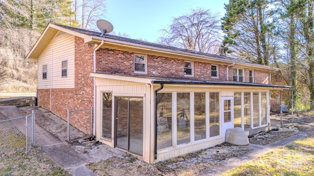 rear view of property featuring a sunroom, fence, and brick siding