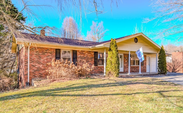 ranch-style house featuring a porch, brick siding, a chimney, and a front yard