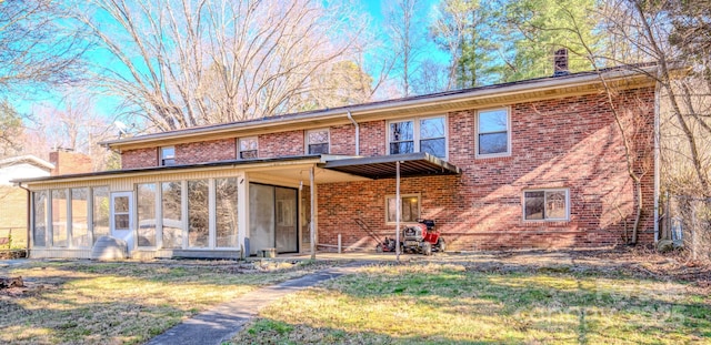 view of front of property with brick siding, a chimney, a front yard, and a sunroom