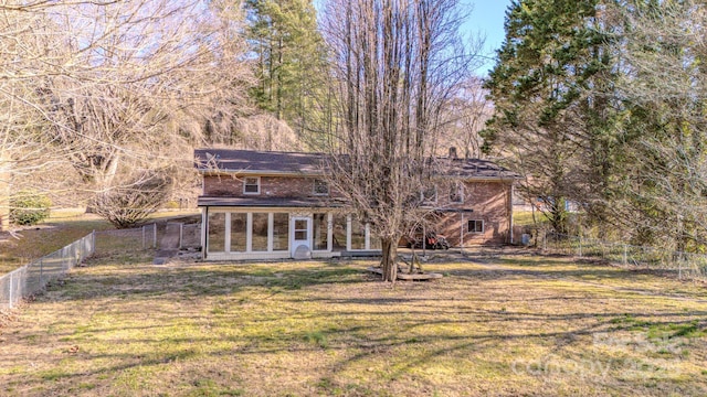 rear view of house featuring a sunroom, a fenced backyard, a lawn, and brick siding