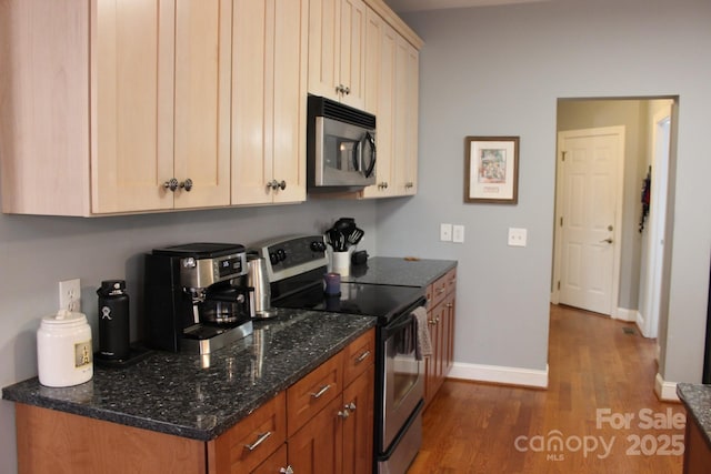 kitchen featuring stainless steel appliances, dark stone countertops, wood finished floors, and baseboards