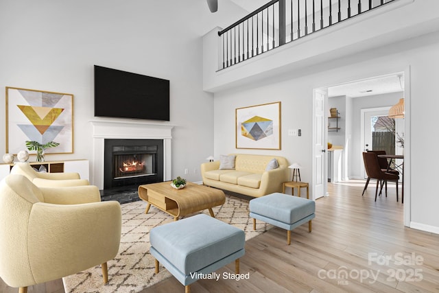 living room featuring baseboards, a lit fireplace, a high ceiling, and wood finished floors