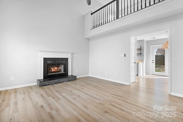 unfurnished living room featuring a towering ceiling, baseboards, wood finished floors, and a stone fireplace