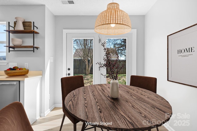 dining room with light wood-type flooring, a textured ceiling, and baseboards