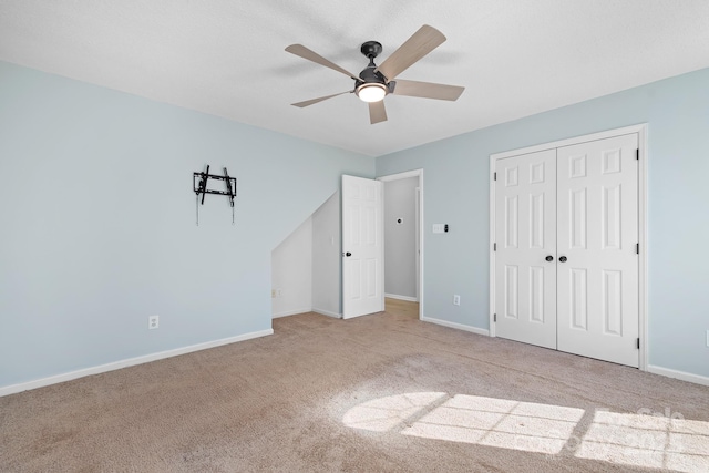 unfurnished bedroom with carpet floors, a closet, baseboards, and a ceiling fan