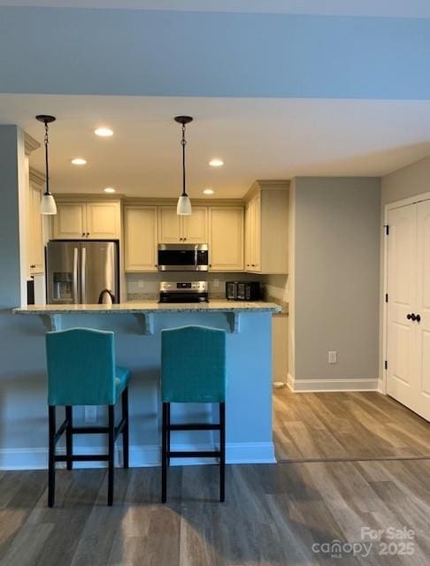 kitchen featuring dark wood-style floors, a kitchen breakfast bar, stainless steel appliances, and decorative light fixtures