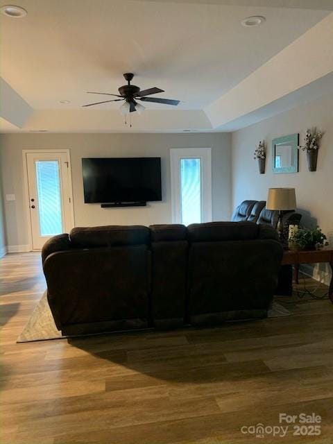 living room featuring a tray ceiling, wood finished floors, a ceiling fan, and baseboards