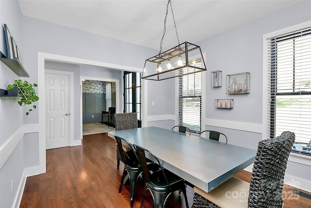 dining space with dark wood-style floors, a textured ceiling, baseboards, and a healthy amount of sunlight