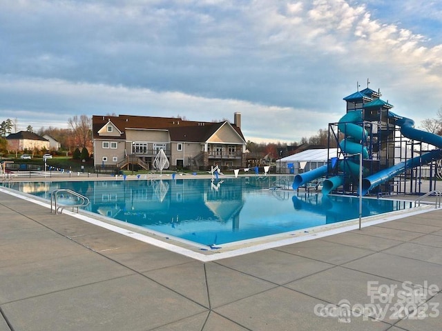 community pool featuring a patio, playground community, and a water slide