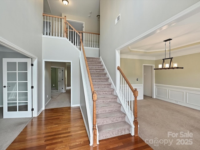 stairway with visible vents, a wainscoted wall, ornamental molding, wood finished floors, and a chandelier