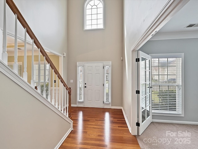 foyer featuring visible vents, wood finished floors, stairway, baseboards, and a towering ceiling