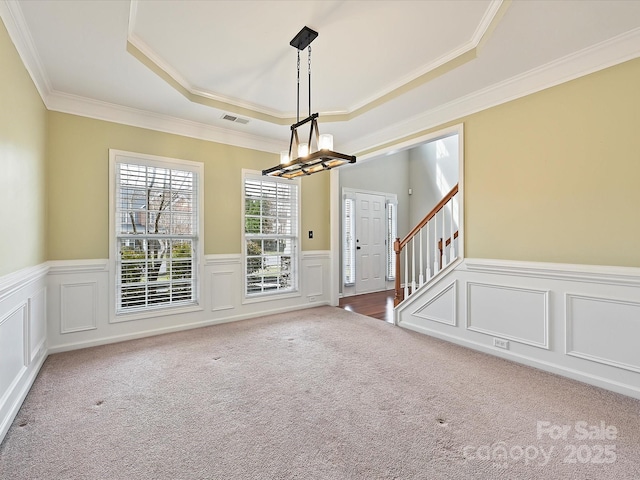 spare room with a wainscoted wall, a notable chandelier, a tray ceiling, carpet floors, and stairs