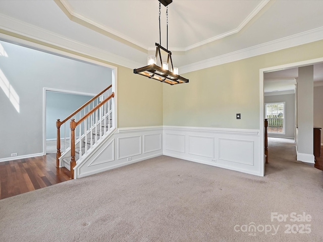 unfurnished dining area with wainscoting, a notable chandelier, ornamental molding, and carpet floors