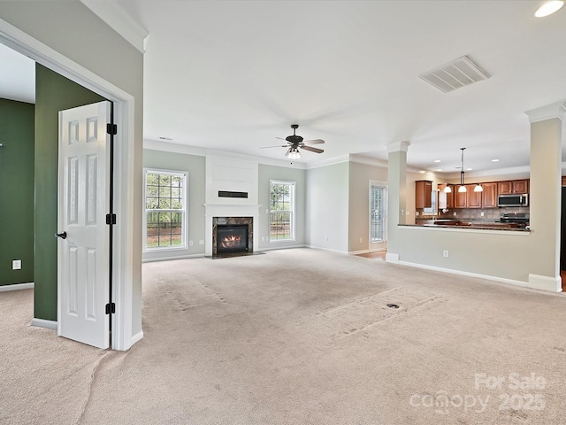 unfurnished living room featuring visible vents, ornamental molding, decorative columns, light colored carpet, and ceiling fan