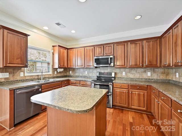 kitchen featuring tasteful backsplash, crown molding, light wood-type flooring, stainless steel appliances, and a sink