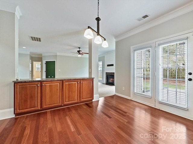 kitchen with brown cabinetry, visible vents, dark wood finished floors, and ornamental molding