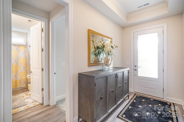 entryway featuring light wood-type flooring, baseboards, visible vents, and a raised ceiling