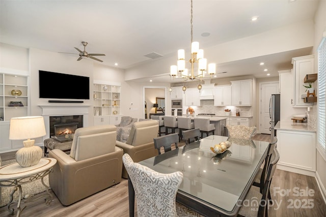 dining area with visible vents, a glass covered fireplace, ceiling fan with notable chandelier, light wood-style floors, and recessed lighting