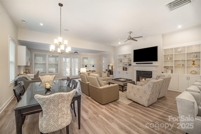 living area with light wood finished floors, a warm lit fireplace, built in features, visible vents, and baseboards