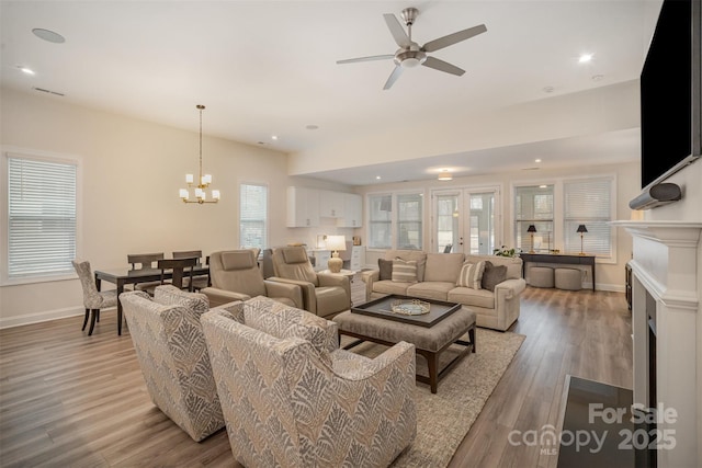 living area featuring visible vents, baseboards, wood finished floors, a fireplace, and ceiling fan with notable chandelier