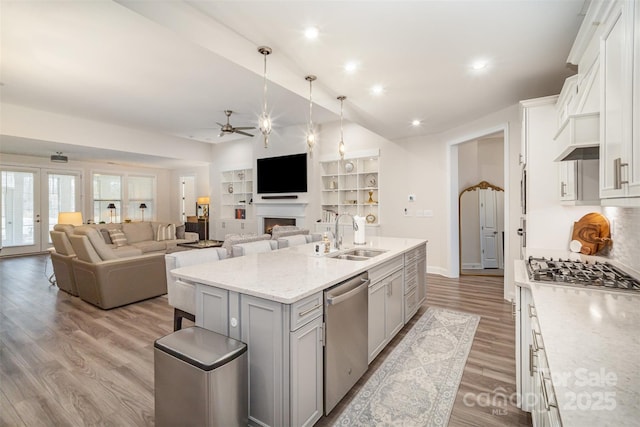 kitchen with a ceiling fan, an island with sink, appliances with stainless steel finishes, light wood-type flooring, and a sink