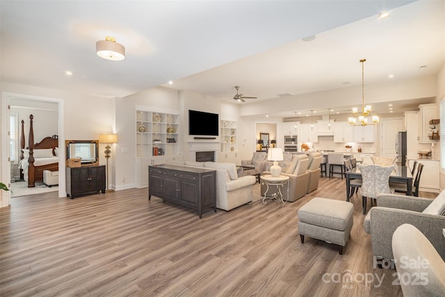 living area featuring ceiling fan with notable chandelier, a fireplace, light wood-style flooring, and recessed lighting