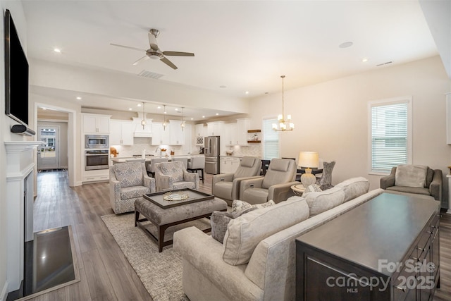 living room with recessed lighting, visible vents, wood finished floors, and ceiling fan with notable chandelier