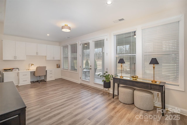 home office featuring light wood-style flooring, a sink, visible vents, baseboards, and built in study area