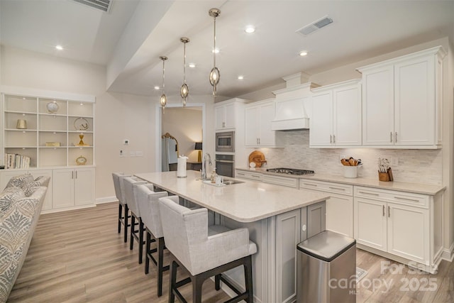 kitchen featuring visible vents, appliances with stainless steel finishes, light wood-style floors, a sink, and premium range hood