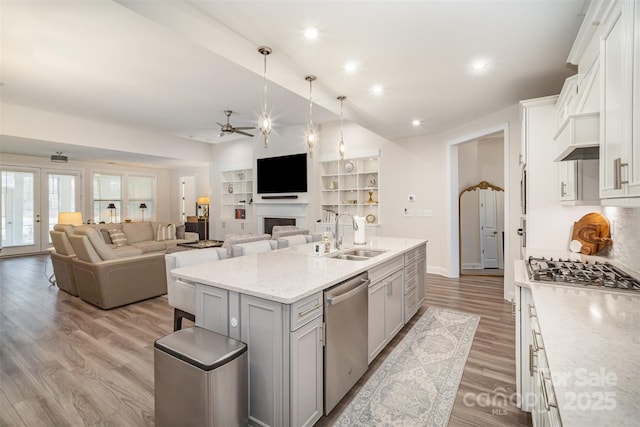 kitchen with a center island with sink, ceiling fan, appliances with stainless steel finishes, light wood-style floors, and a sink