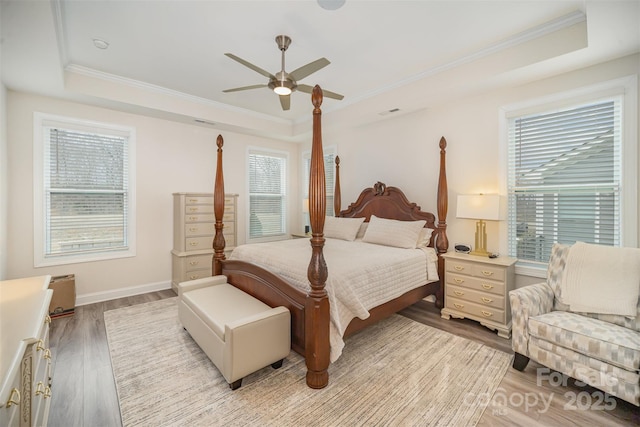 bedroom with light wood-style floors, a raised ceiling, and ornamental molding