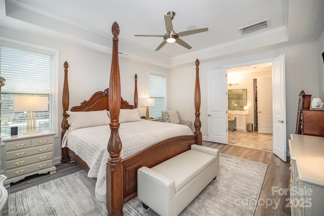 bedroom featuring a raised ceiling, visible vents, crown molding, and wood finished floors