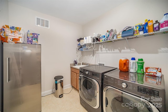 washroom with cabinet space, visible vents, a sink, washer and dryer, and baseboards