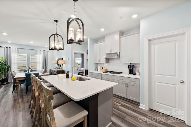 kitchen featuring backsplash, a kitchen island with sink, under cabinet range hood, gas stovetop, and a sink