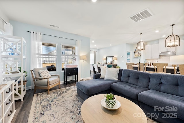 living room with dark wood finished floors, visible vents, and a notable chandelier