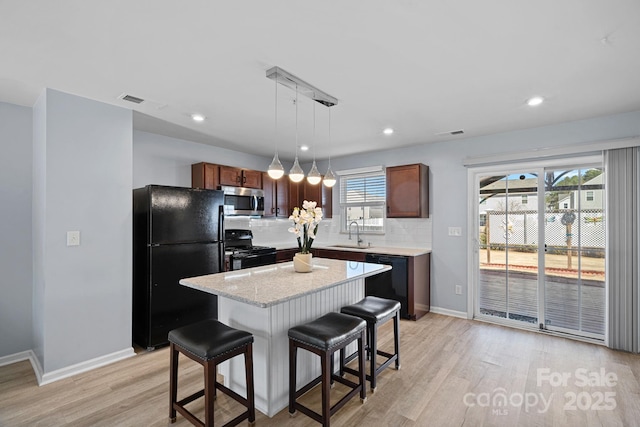 kitchen with decorative backsplash, light wood-style floors, a sink, black appliances, and a kitchen breakfast bar