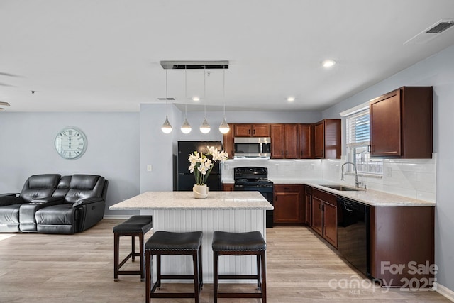 kitchen with a sink, light wood-style floors, black appliances, tasteful backsplash, and a kitchen bar