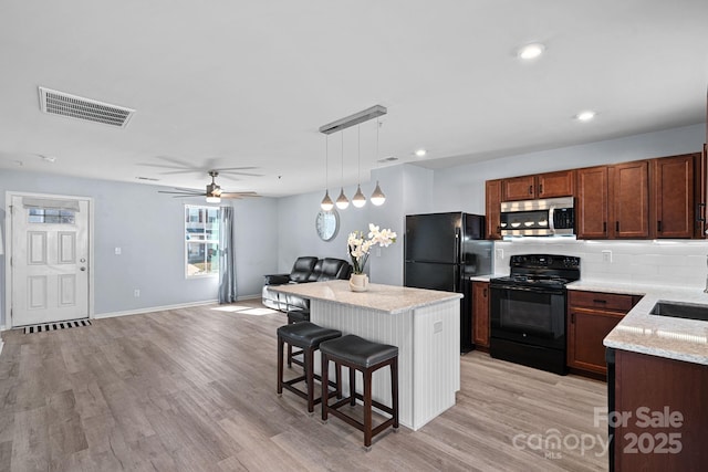 kitchen featuring light wood finished floors, visible vents, a center island, black appliances, and a kitchen bar