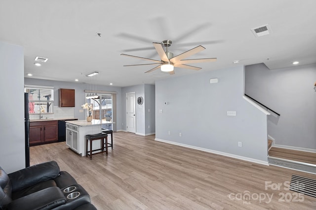 living area with light wood-style flooring, a ceiling fan, visible vents, baseboards, and stairway