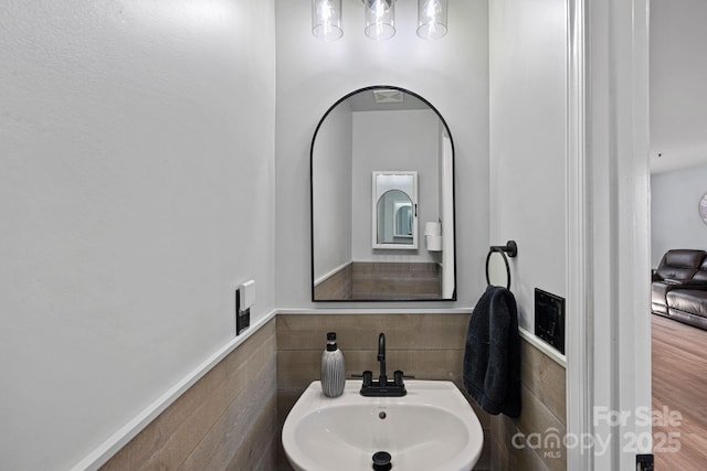 bathroom featuring wainscoting, a sink, and tile walls